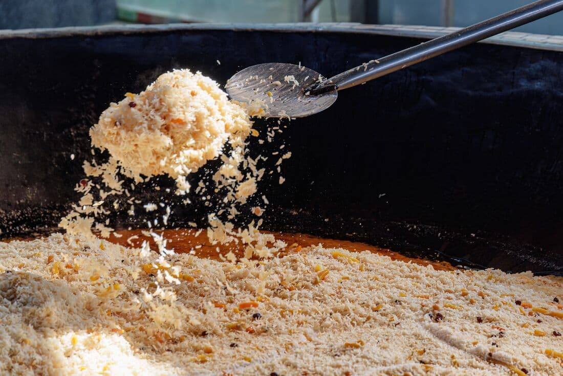 A chef turns rice in a cooking pan of plov, a traditional Uzebk pilaf, with a huge spoon