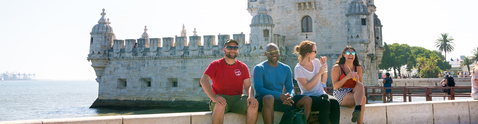 Intrepid Travel group sitting on river bank in front of Belem Tower, Lisbon, Portugal