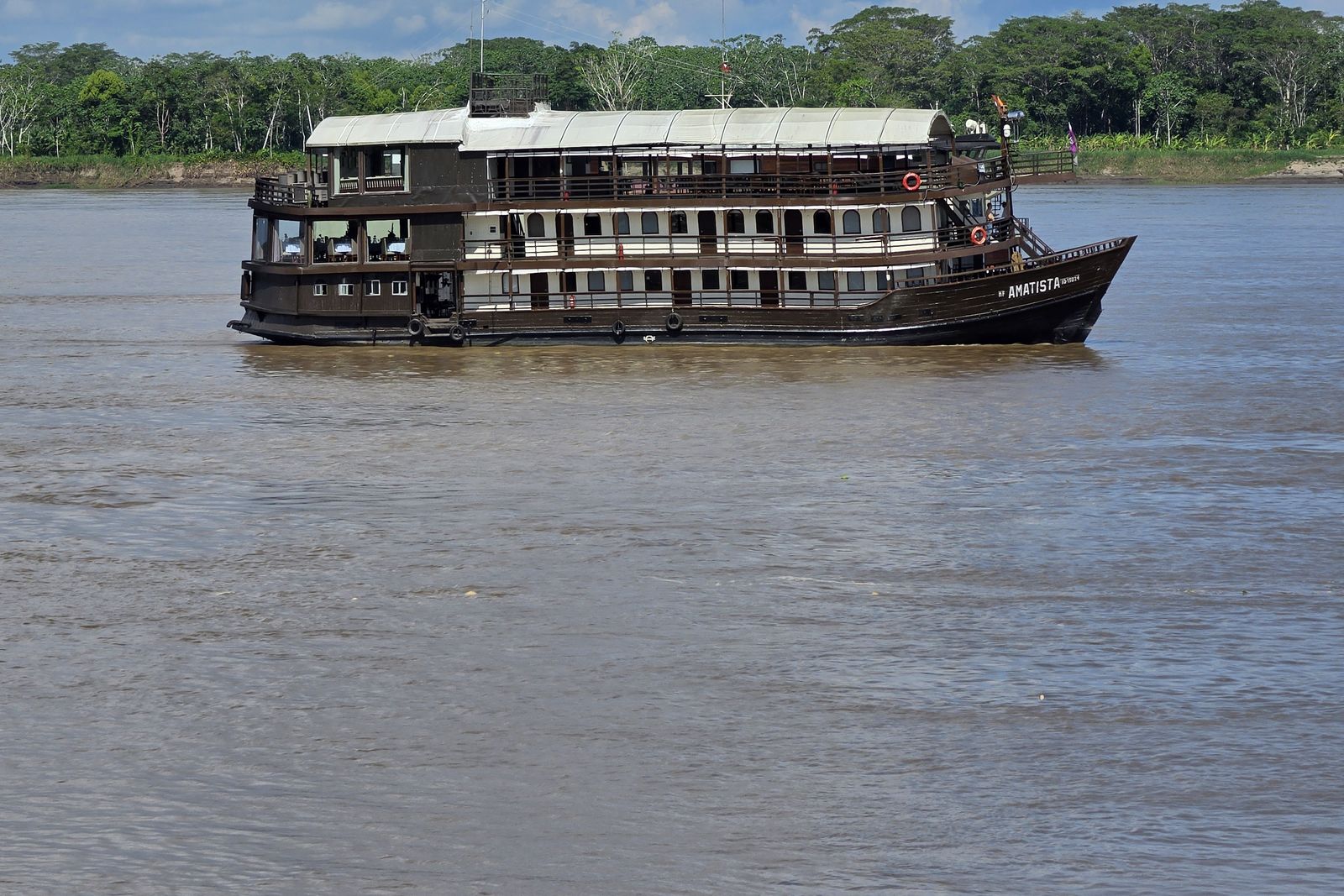 A multi-deck river boat on the wide, brown Amazon under a cloudy sky.